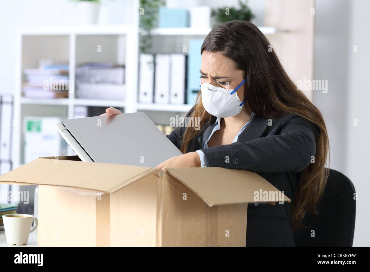 Sad fired executive woman with protective mask crying packing her stuff on a box at the office Stock Photo