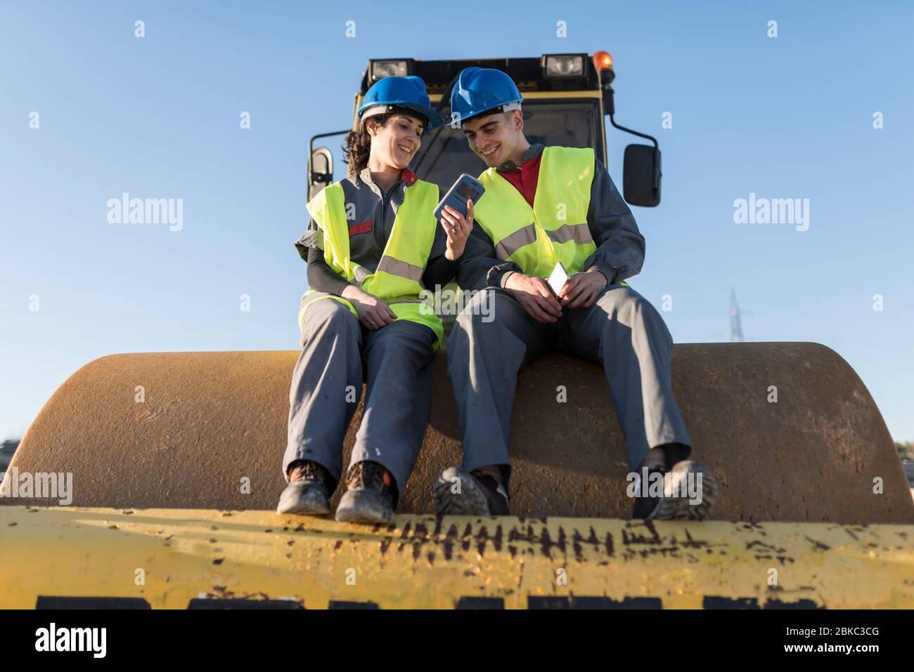 Couple of workers taking a break in their job and looking telephone on steamroller bulldozer Stock Photo