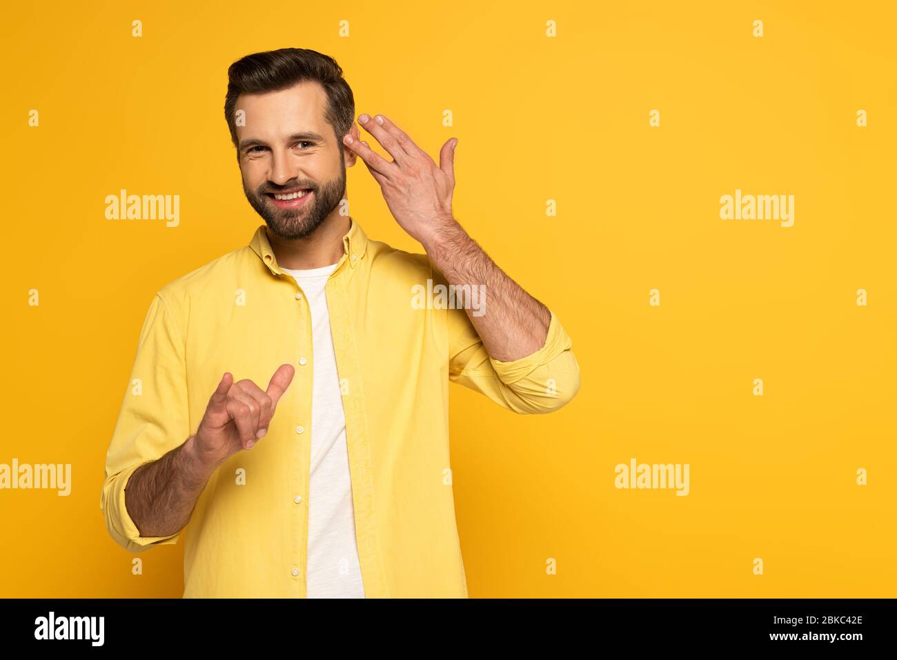 Smiling man looking at camera while using deaf and dumb language on yellow background Stock Photo
