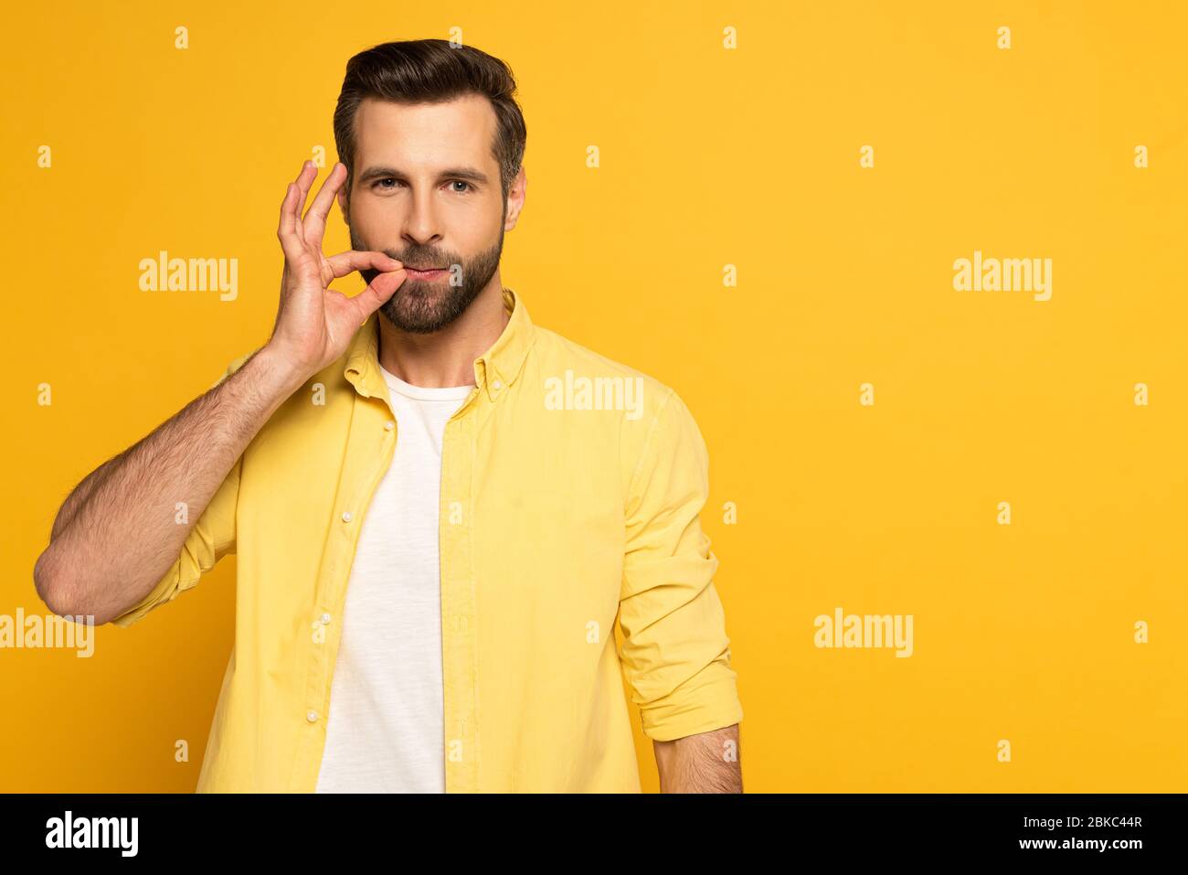 Handsome man using sign language and looking at camera on yellow background Stock Photo