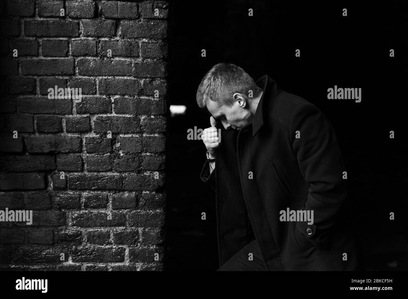 Serious man in the coat standing with a tilted head in front of the wall  Stock Photo