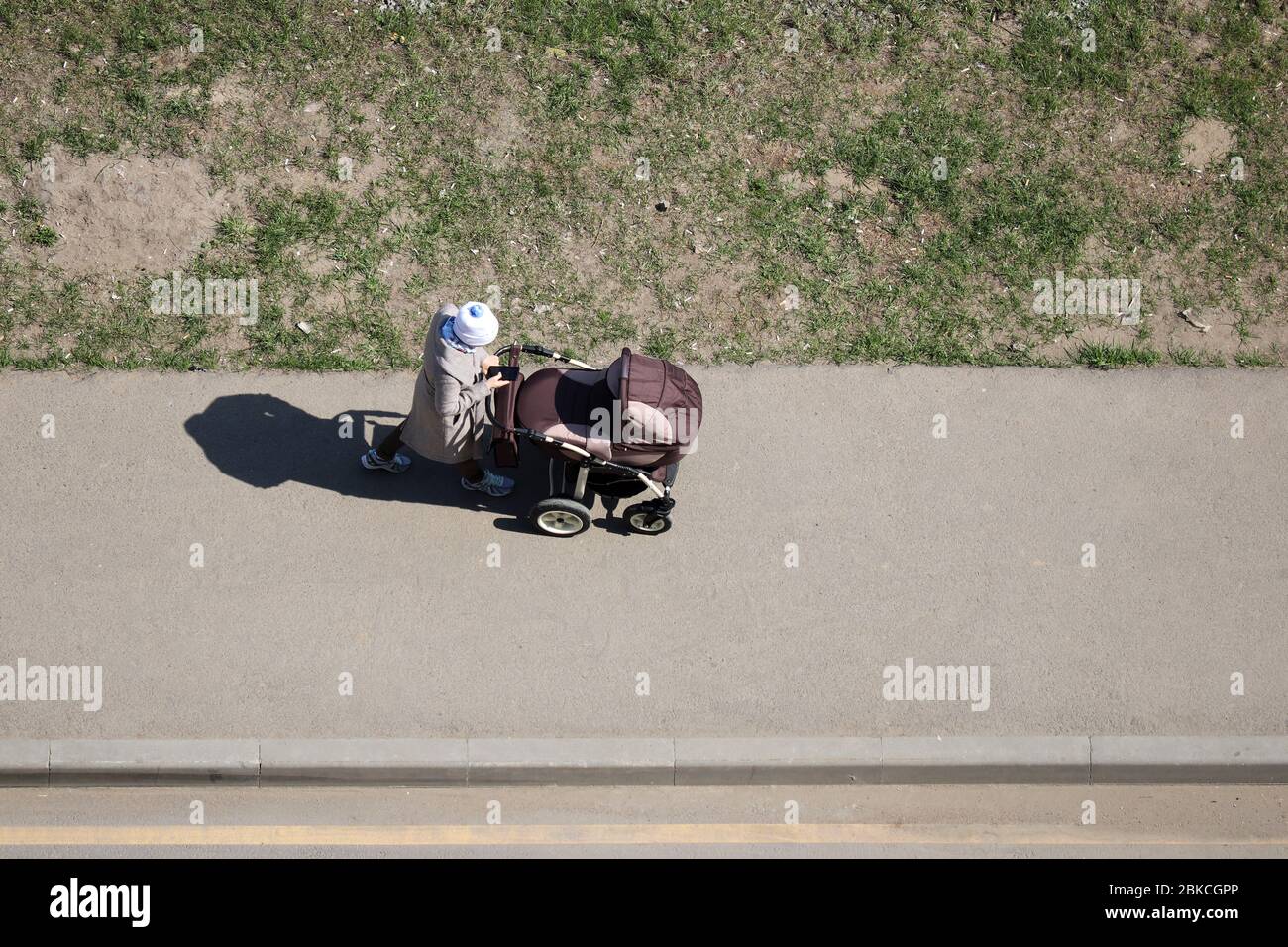 Woman with a baby stroller walking on a spring street. Quarantine in a city during covid-19 coronavirus pandemic, concept of motherhood, single mom Stock Photo