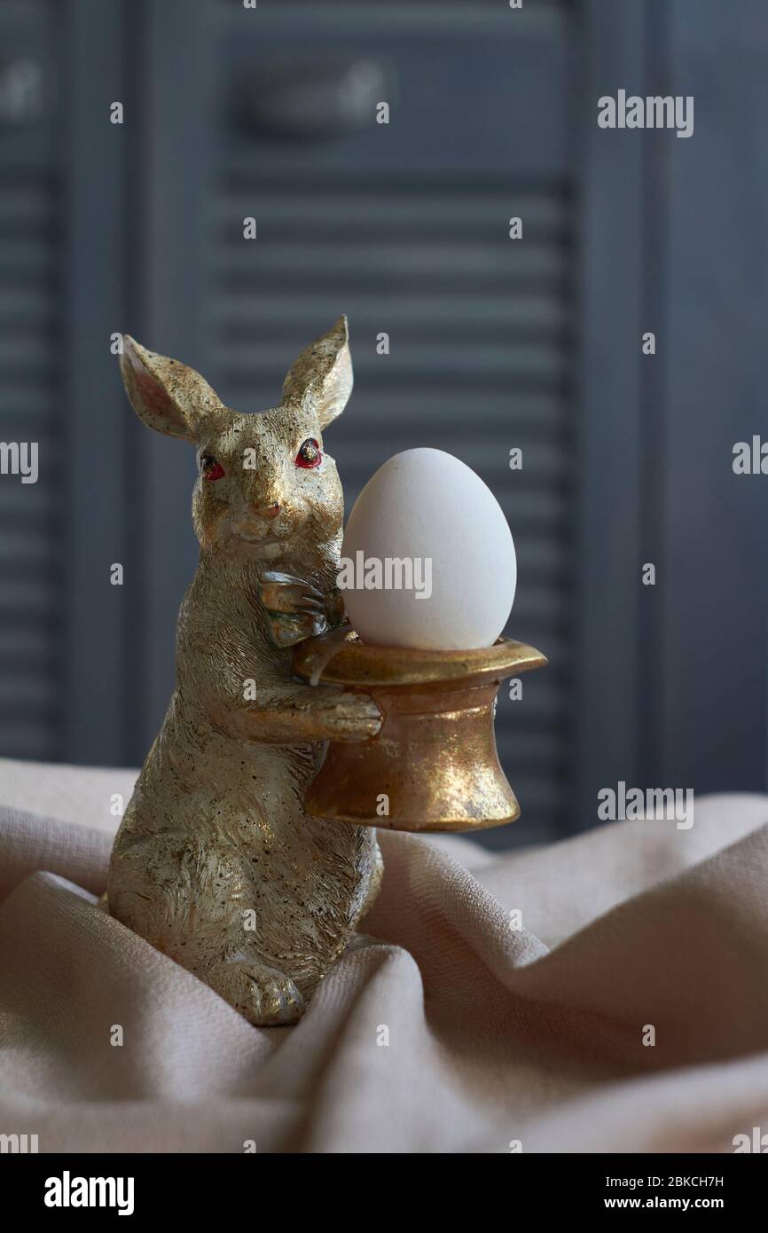 Spring composition, golden rabbit figurine with egg on beige tablecloth, Easter concept, selective focus Stock Photo