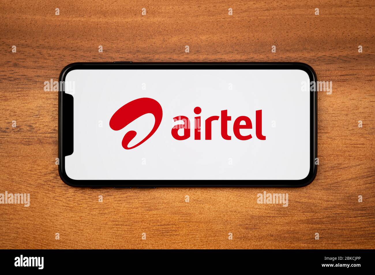 A smartphone showing the Bharti Airtel logo rests on a plain wooden table (Editorial use only). Stock Photo