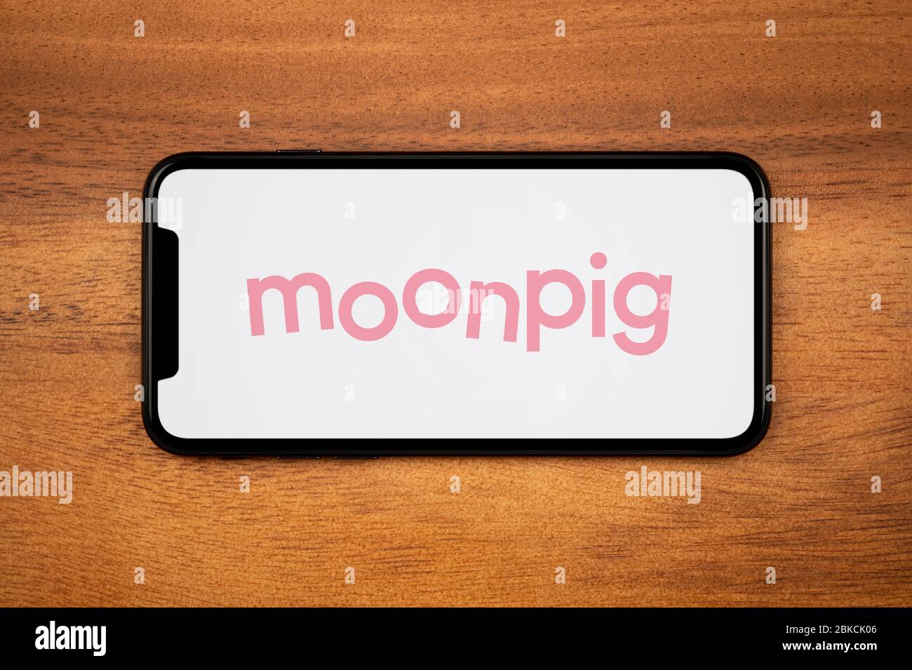 A smartphone showing the Moonpig logo rests on a plain wooden table