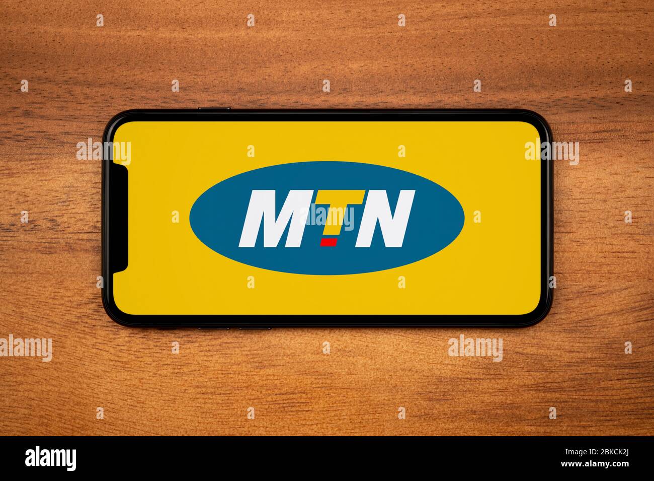 A smartphone showing the MTN logo rests on a plain wooden table (Editorial use only). Stock Photo