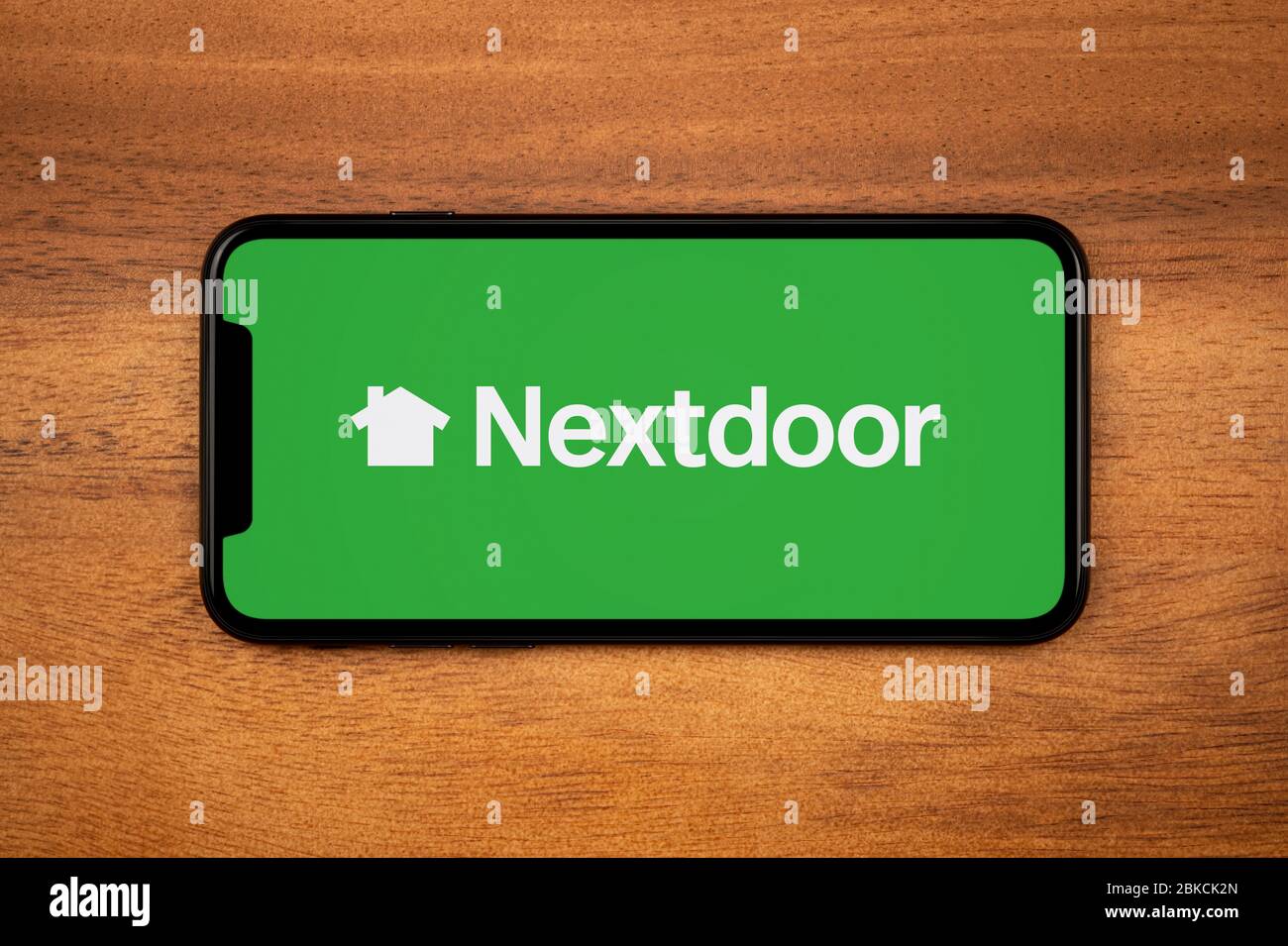 A smartphone showing the Nextdoor logo rests on a plain wooden table (Editorial use only). Stock Photo