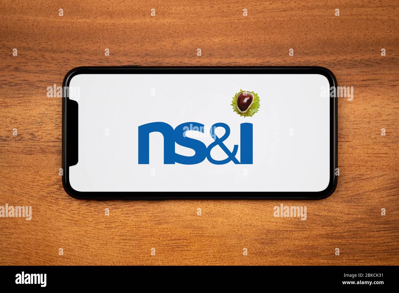 A smartphone showing the NS&I logo rests on a plain wooden table (Editorial use only). Stock Photo