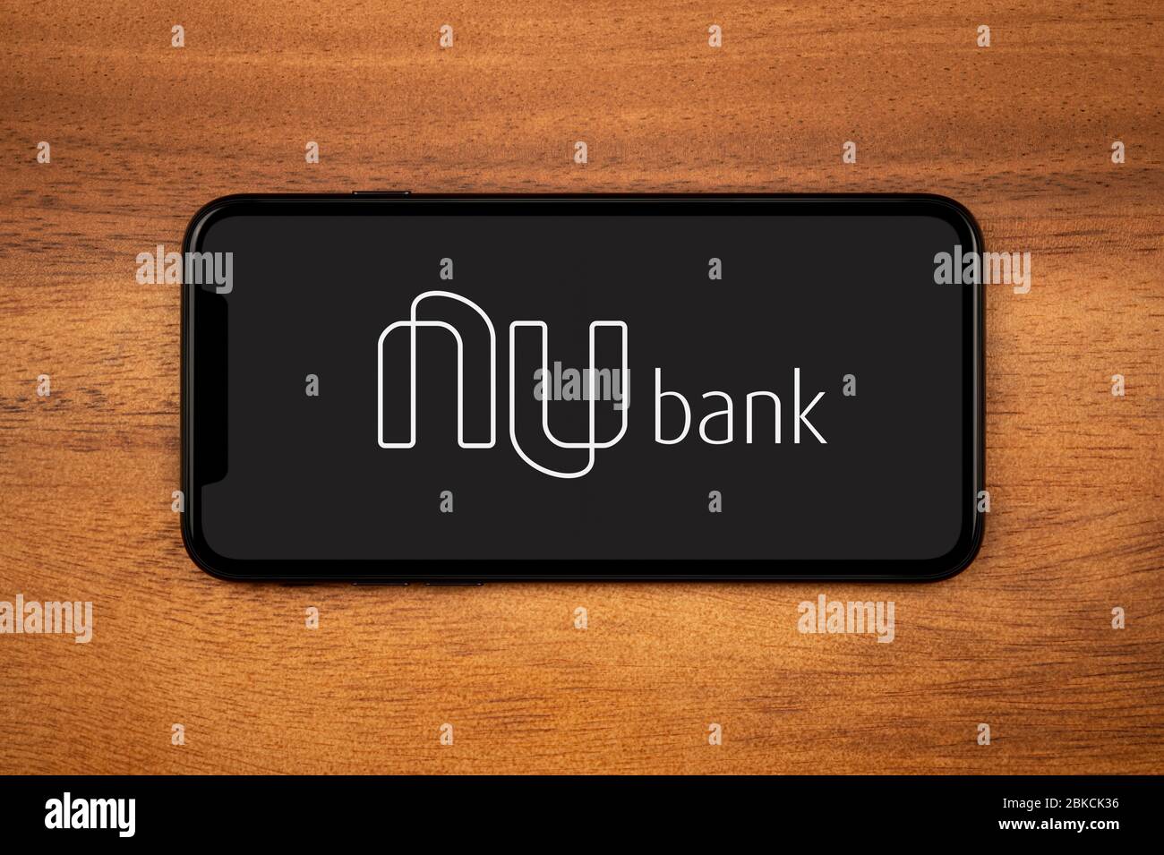 A smartphone showing the Nu Bank logo rests on a plain wooden table (Editorial use only). Stock Photo