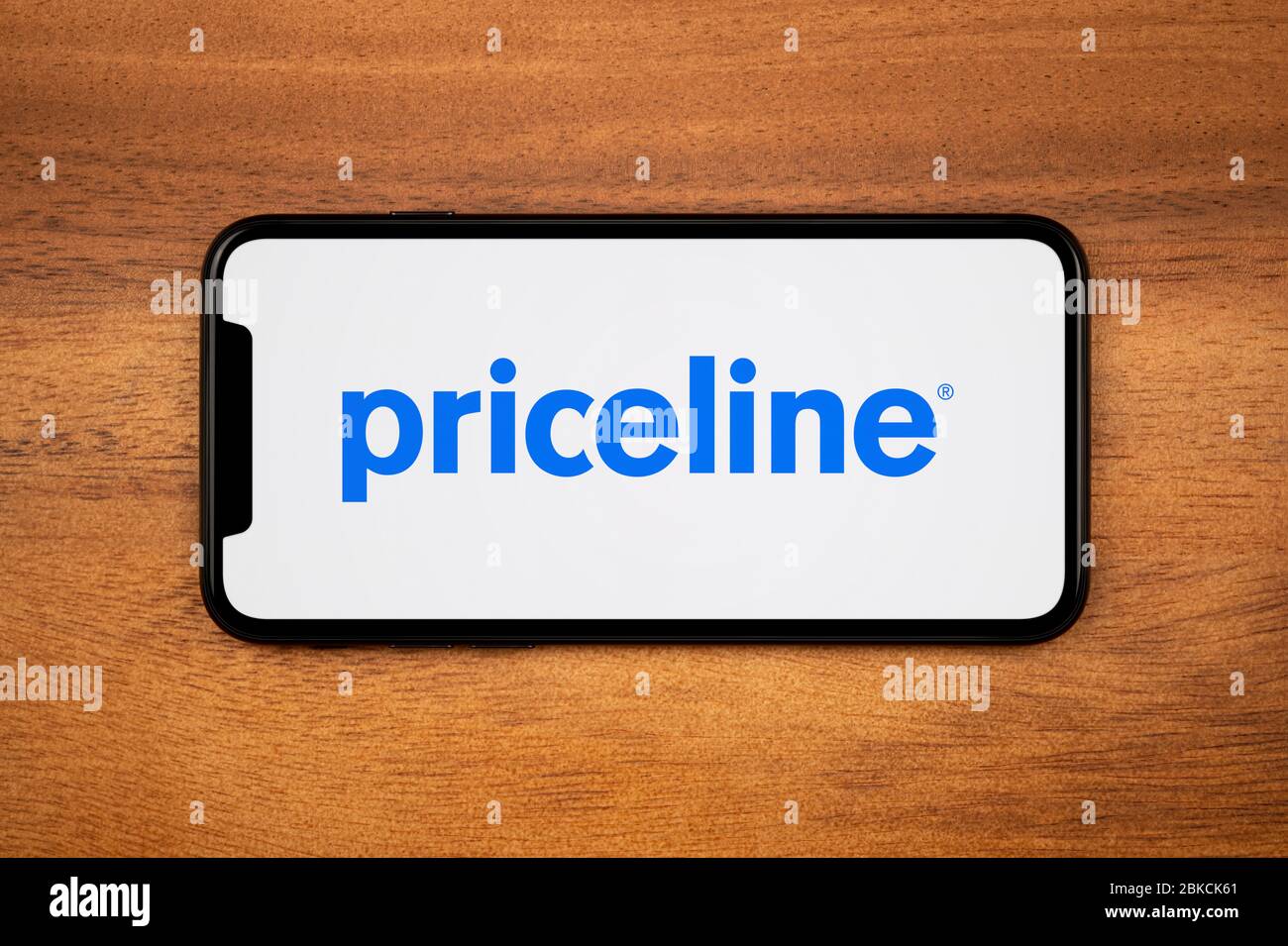 A smartphone showing the Priceline logo rests on a plain wooden table