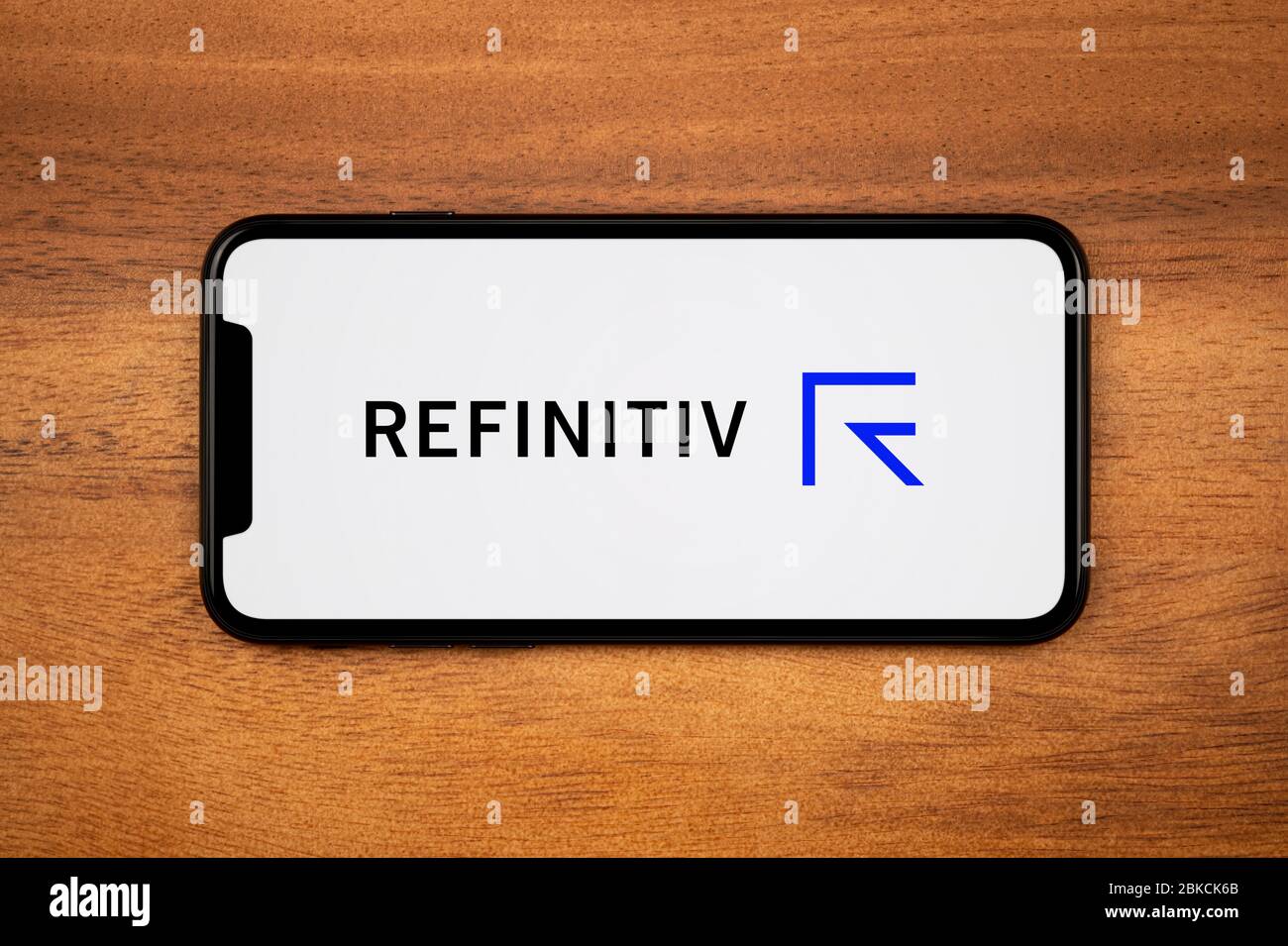 A smartphone showing the Refinitiv logo rests on a plain wooden table (Editorial use only). Stock Photo
