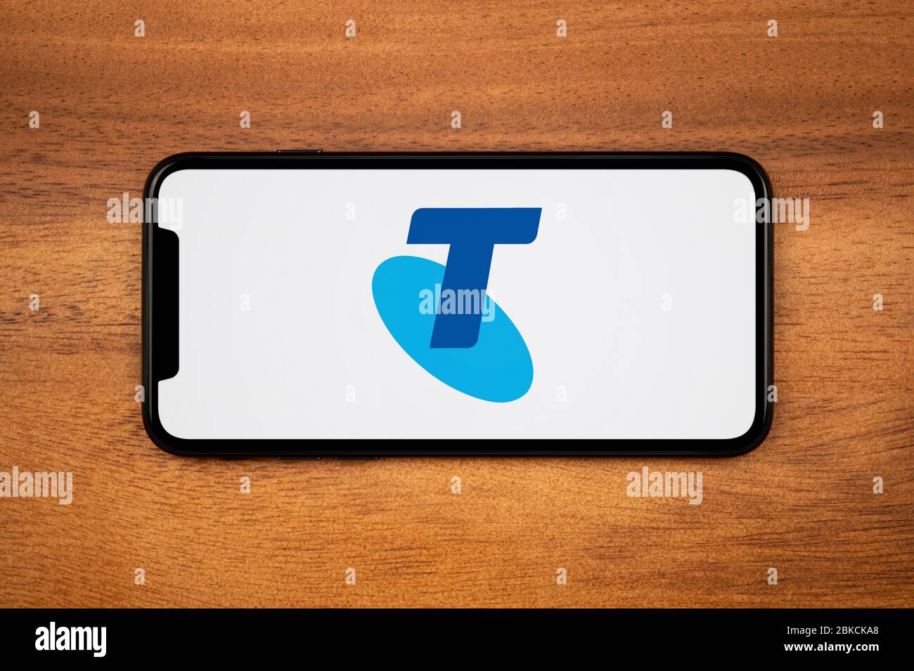 A smartphone showing the Telstra logo rests on a plain wooden table (Editorial use only). Stock Photo