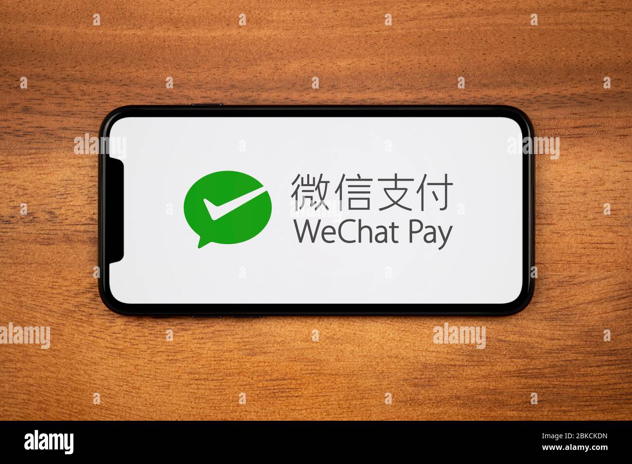 A smartphone showing the WeChat Pay logo rests on a plain wooden table (Editorial use only). Stock Photo