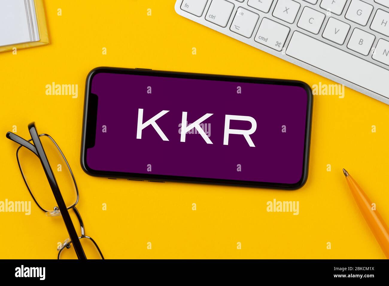 A smartphone showing the KKR logo rests on a yellow background along with a keyboard, glasses, pen and book (Editorial use only). Stock Photo