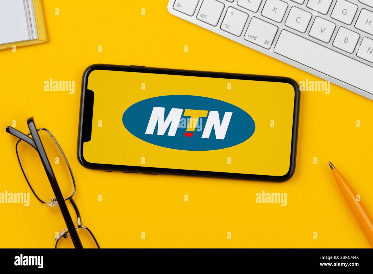 A smartphone showing the MTN logo rests on a yellow background along with a keyboard, glasses, pen and book (Editorial use only). Stock Photo