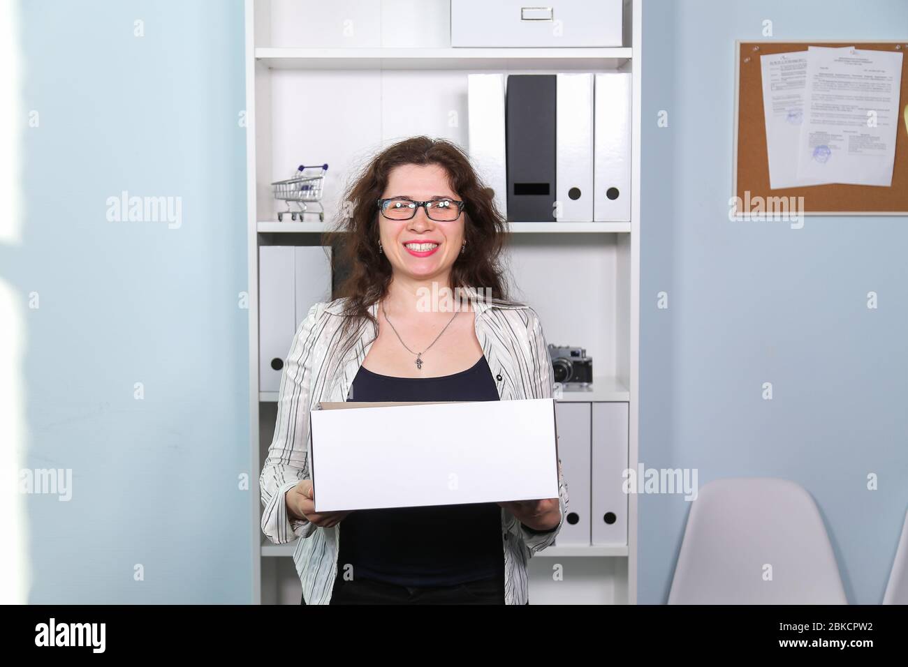 Concept of dismissal from work. Happy woman with carton box with her stationery stuff, girl was fired from her job. Stock Photo