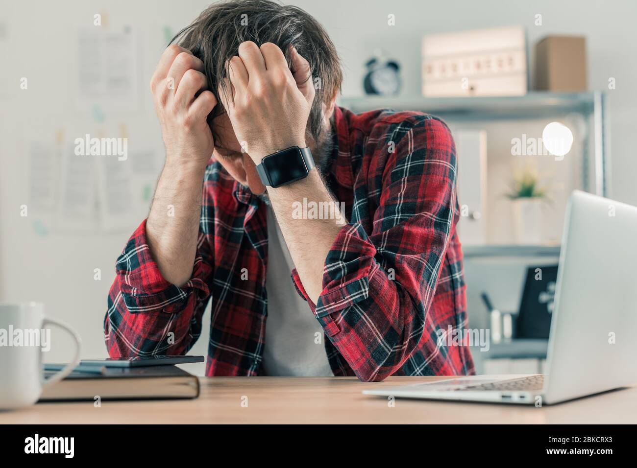 Disappointed freelancer at home office with his head in hands, selective focus Stock Photo