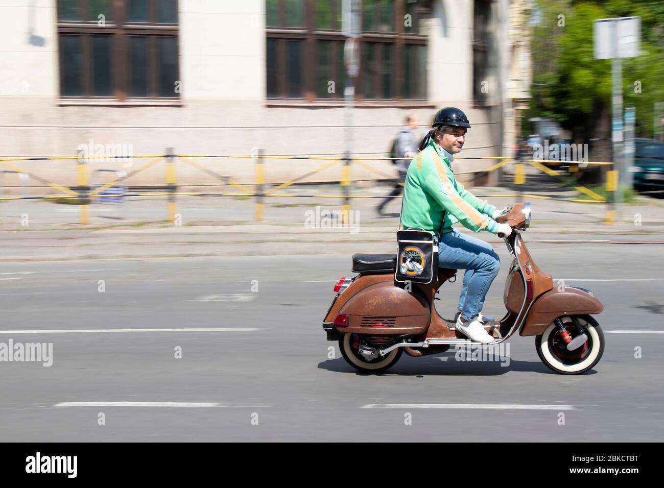 Belgrade, Serbia - April 24, 2020: Mature man in retro outfit riding vintage scooter vespa on empty city street in Dorcol area, on a sunny day Stock Photo