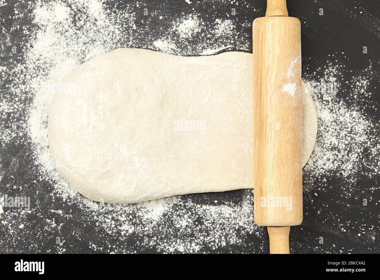 Dough and wood rolling pin on clean black background top view Stock