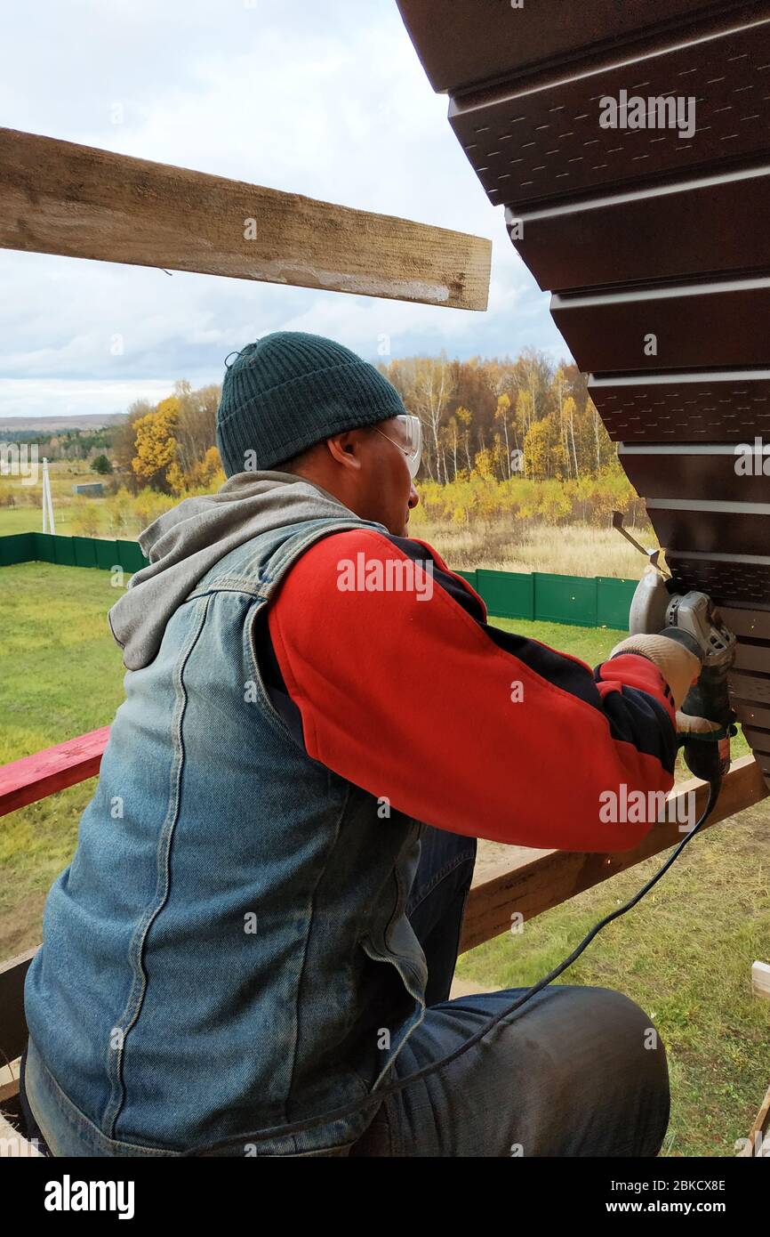 Worker trims the metal sheet of the roof.2020 Stock Photo