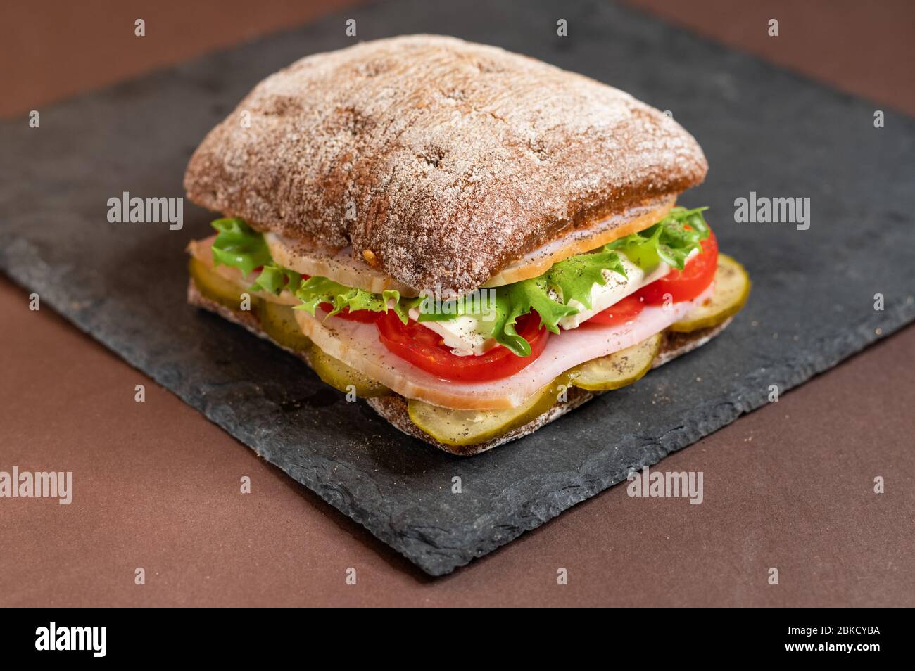 A sandwich on a tray. Sandwich with meat and vegetables on a black granite stand. Special square roll for sandwiches. Stock Photo