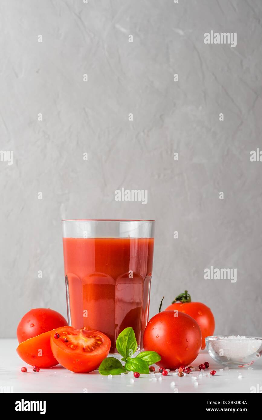 Tomato juice in a glass with fresh tomatoes, basil, salt and pepper on white marble table. vertical orientation Stock Photo