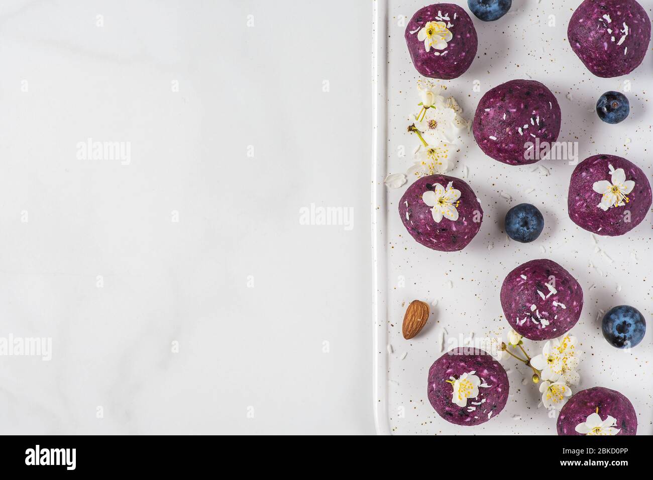 Raw vegan energy balls or bites made of blueberry, acai, nuts and dates served with flowers. top view with copy space. Food styling. Healthy dessert Stock Photo