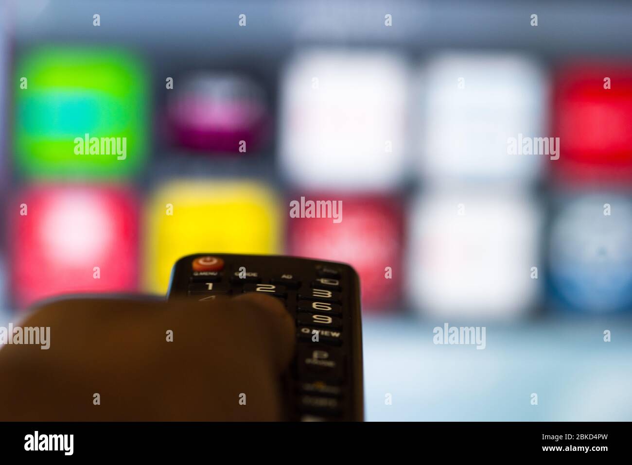 Person operating smart TV remote with television apps in background Stock Photo