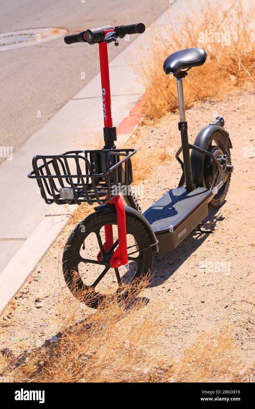An abandoned electric scooter sits amongst the weeds and dust in an empty Tucson city during the Covid-19 lockdown Stock Photo