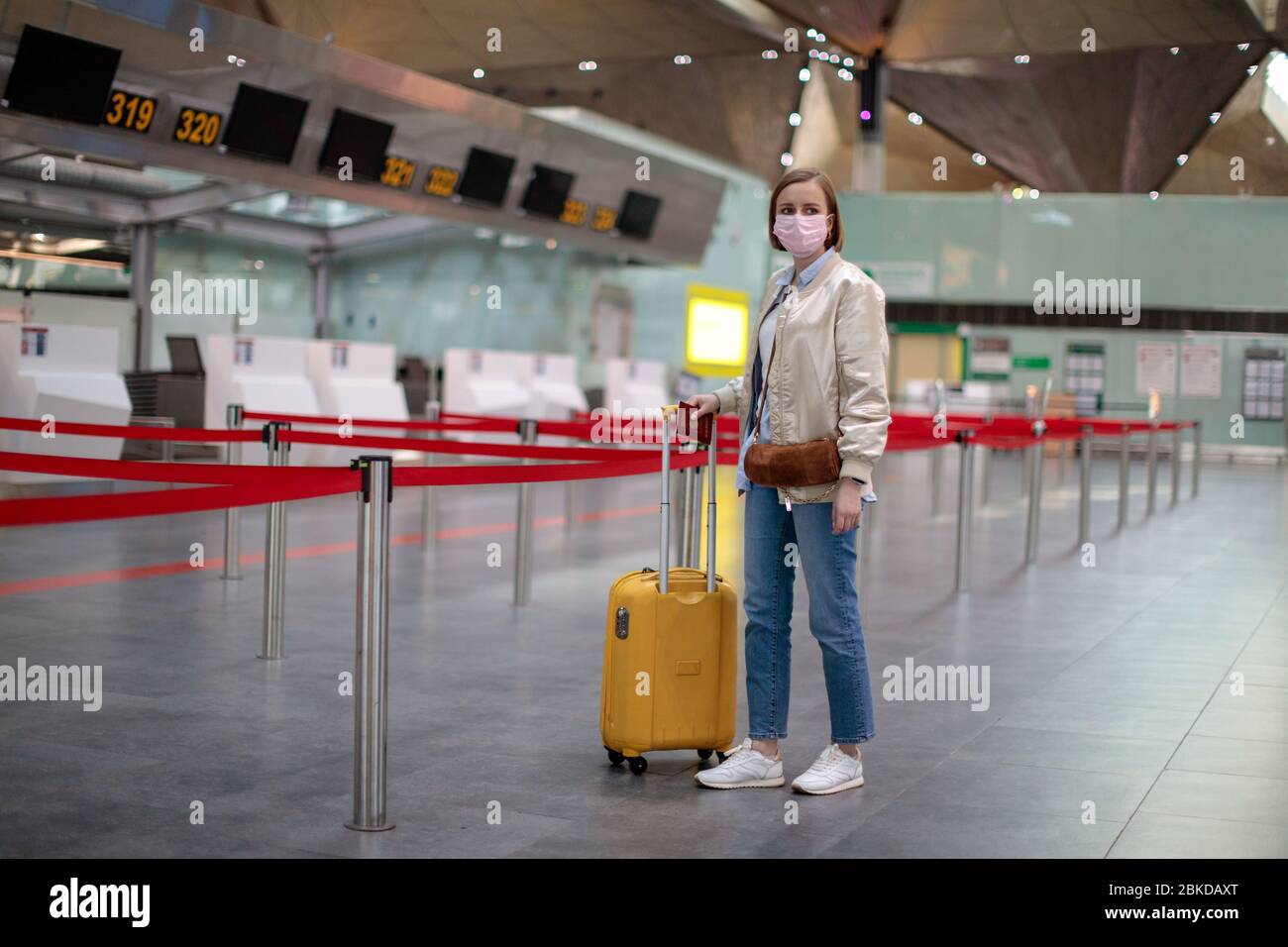 Woman with luggage stands at almost empty check-in counters at the airport terminal due to coronavirus pandemic/Covid-19 outbreak travel restrictions. Stock Photo