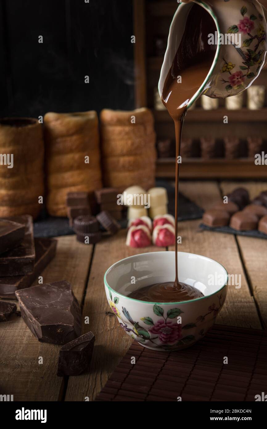 Small pieces of different flavours of chocolate. Melted chocolate falls in a porcelain bowl Stock Photo
