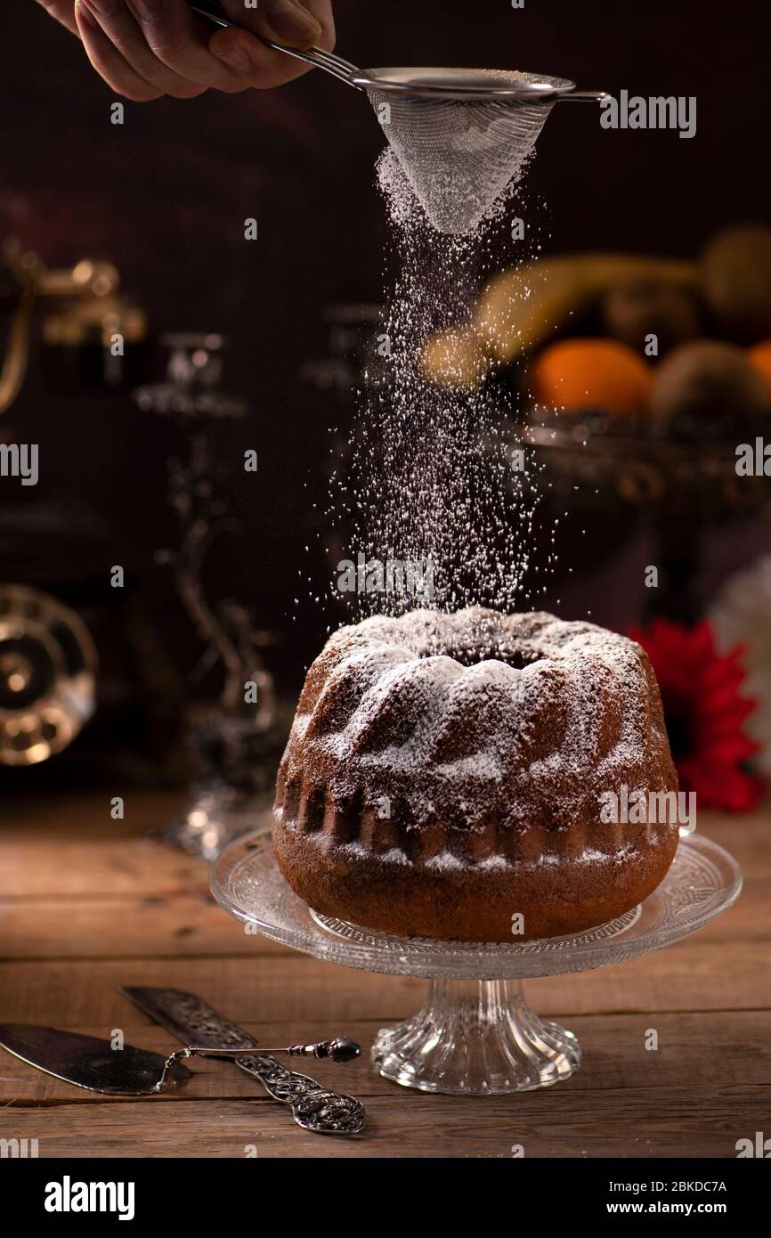 Cake with banana flavour on a wooden table throwing sugar powder on it Stock Photo