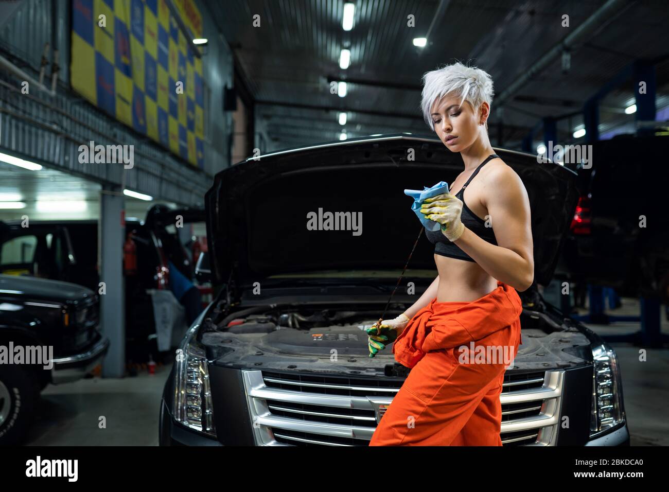 Girl mechanic checks engine oil. Scheduled oil change in the car. Car service. Stock Photo
