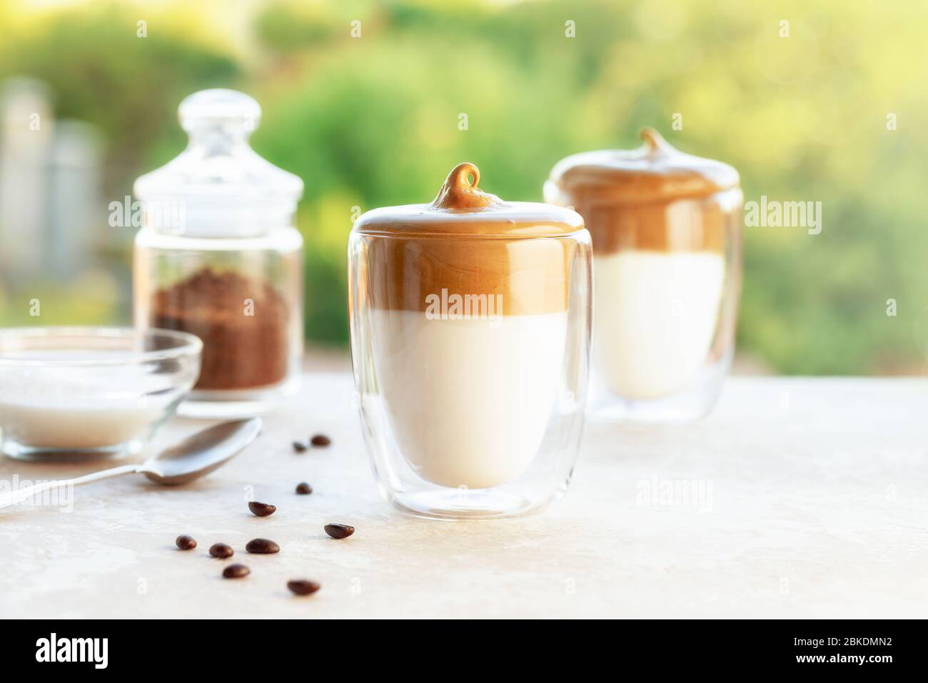 Tasty homemade Dalgona coffee in glass cup with ingredients, coffee and suger on a table on green background. Recipe popular Korean drink latte with f Stock Photo