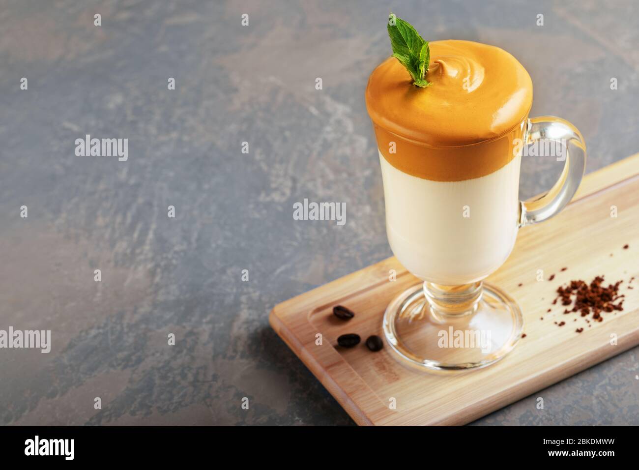 Homemade Dalgona coffee in glass cup on wooden board on grey background. Trend korean Iced  latte coffee drink with foam of instant coffee with coffee Stock Photo