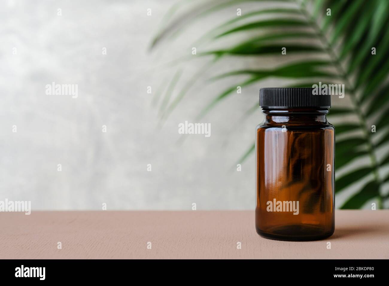 Clear empty pill bottle with tropical leaf. Transparent medicine bottle of brown glass mockup. Stock Photo