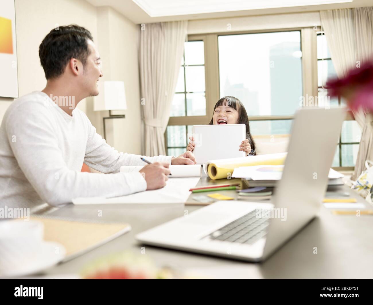 young asian man freelance designer taking care of child while working from home (artwork in background digitally altered) Stock Photo