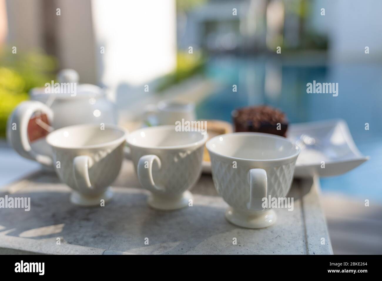 Close up. Afternoon tea set with hot tea, chocolate brownie, cup cake and vanila icecream on table around swimming pool in hotel resort background. Stock Photo