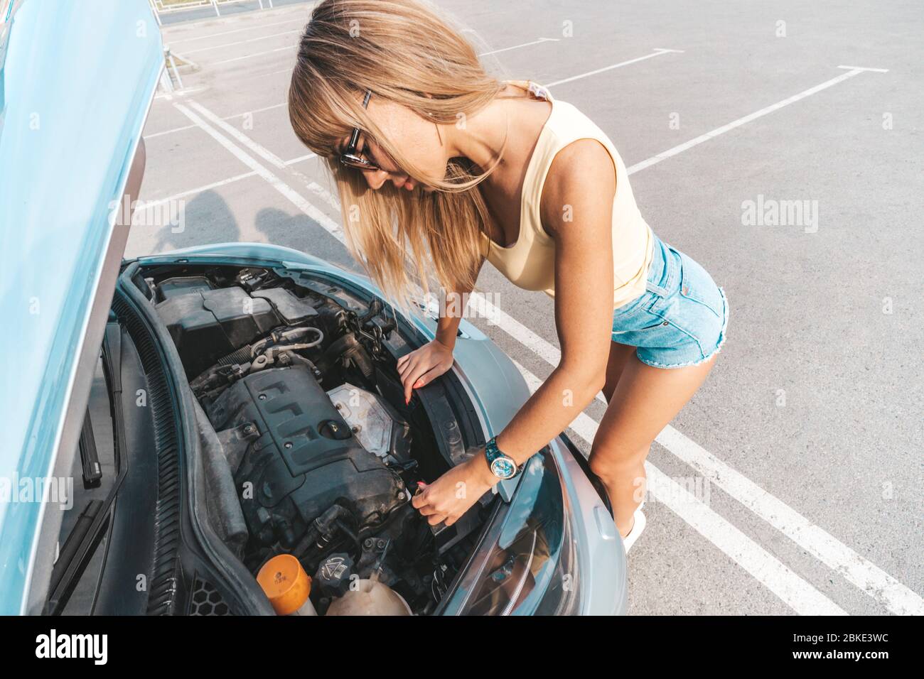 Woman opened hood of her auto that stopped on road and checking level of machine oil. Car breakage. Stock Photo