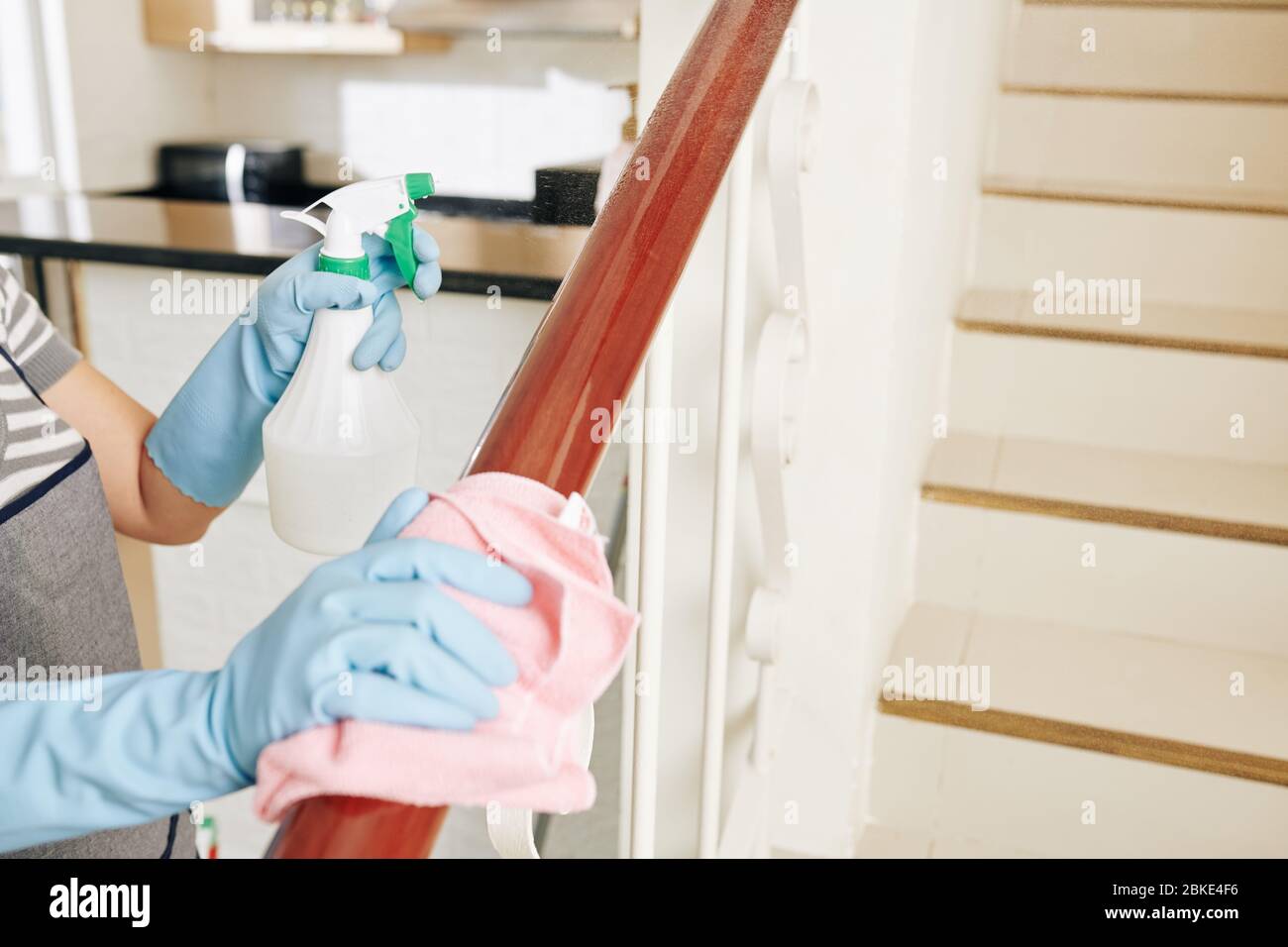 Woman spraying stair railing with cleaning detergent and wiping off