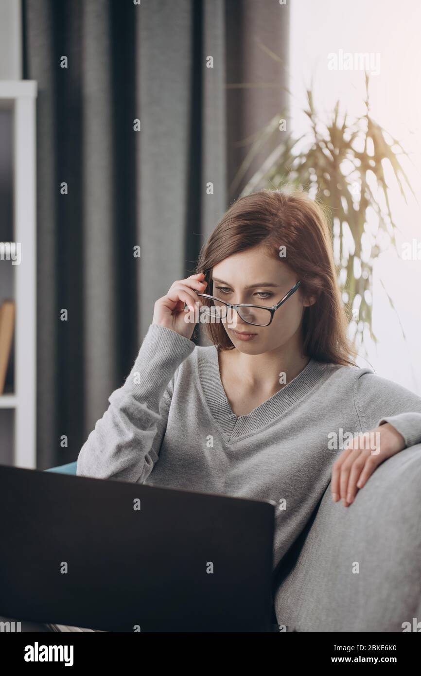 Serious dark-haired woman using laptop for remote work Stock Photo