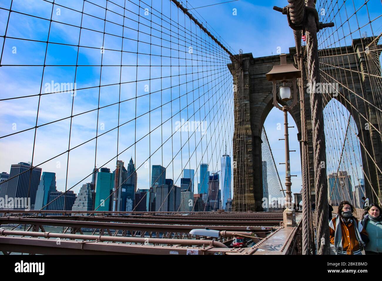 Crossing Brooklyn Bridge with tourists sightseeing and a view of the skyline of Lower Manhattan with the One World Trade Center. Stock Photo