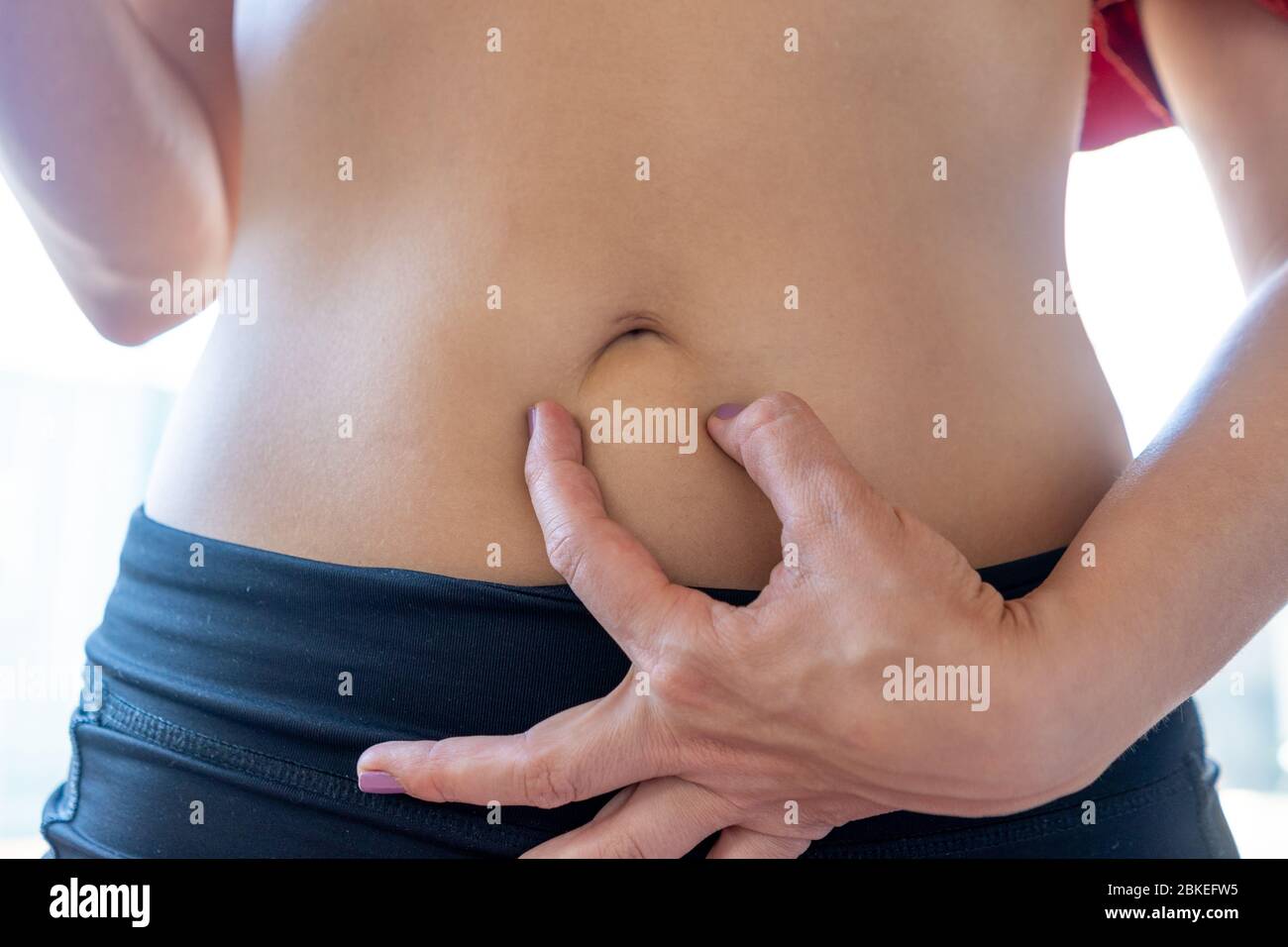 Young woman holding with her fingers her belly button to create a sad mouth Stock Photo