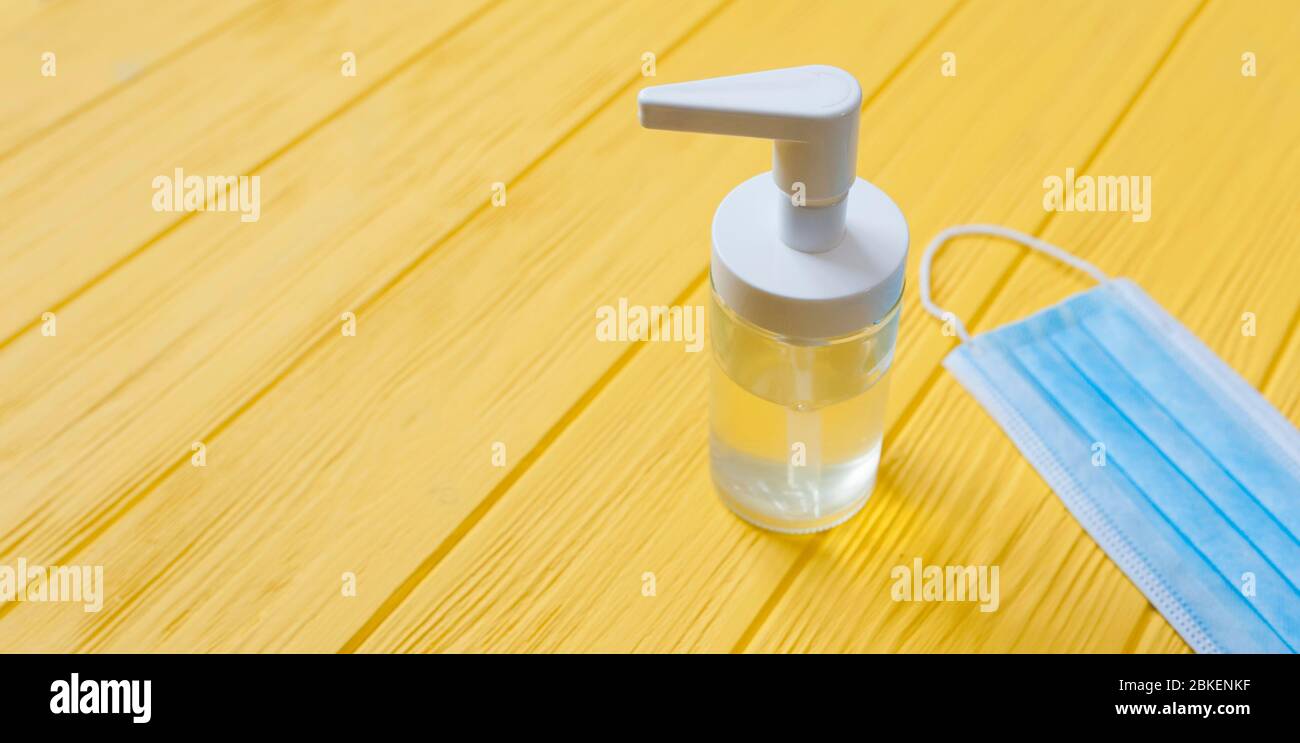 Hand sanitizer bottle and respiratory face mask on yellow wooden background. Stop coronavirus concept banner. Using antibacterial gel for hands during Stock Photo