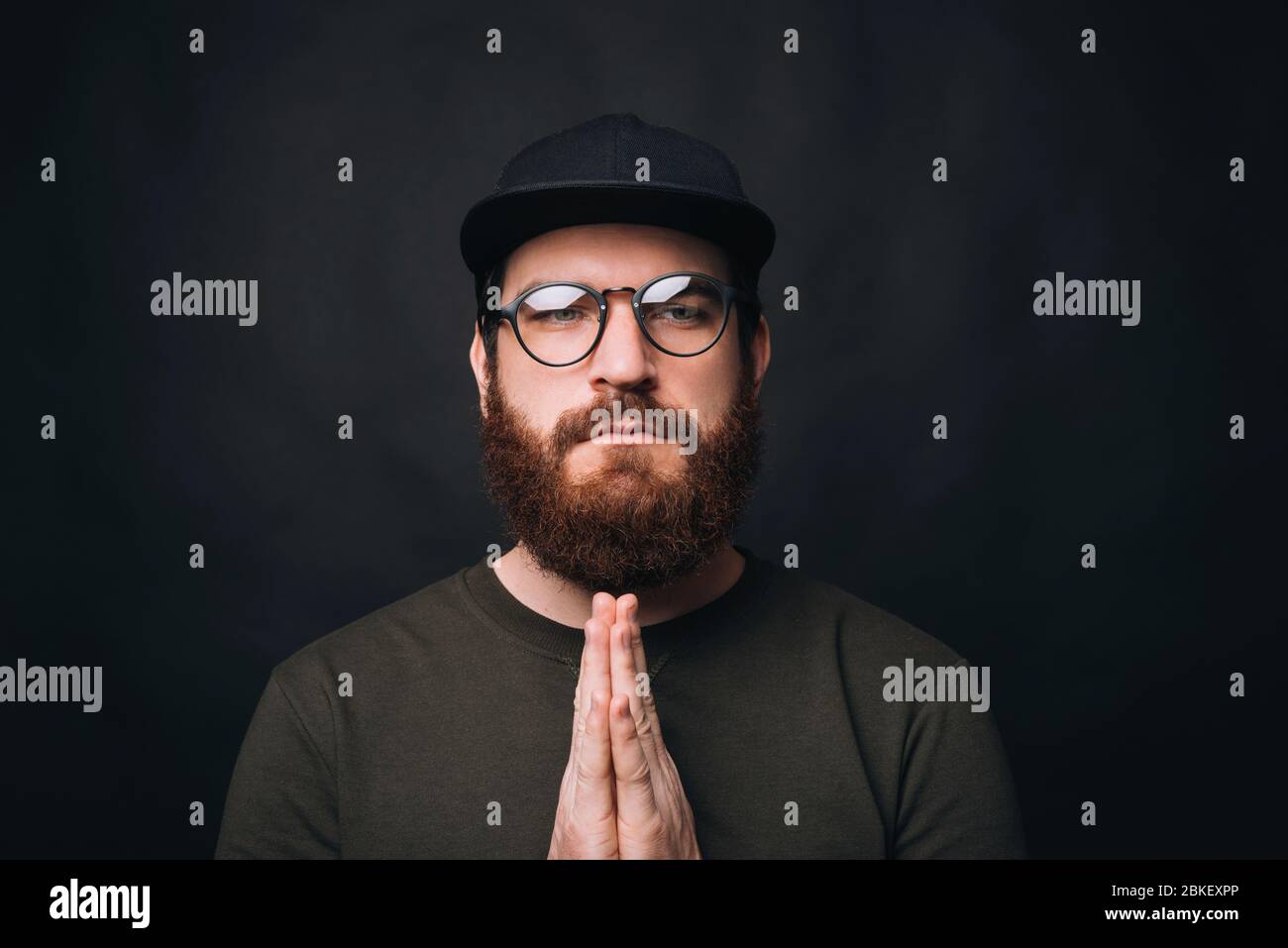 Close up portrait of a serious man holding hands together praying with