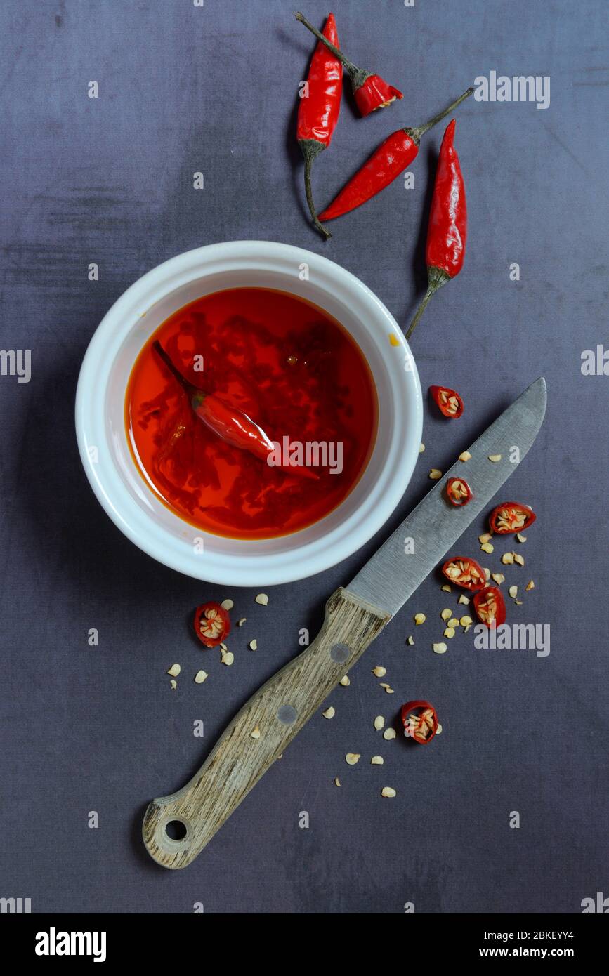 Chili oil in bowl with knife and chili peppers, food photography, studio shot, Germany Stock Photo