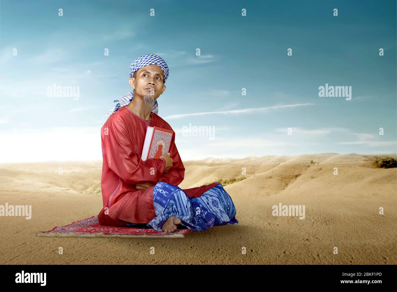 Asian Muslim man sitting and holding the Quran on the desert Stock Photo