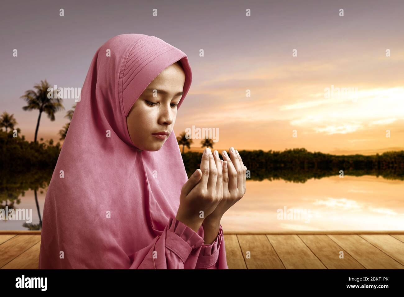 Asian Muslim woman in a veil standing while raised hands and praying ...