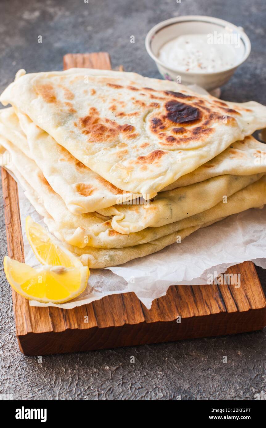 Homemade flatbread stuffed with potato, herbs and cheese with yogurt sauce and lemon. Close up and overhead view. Stock Photo