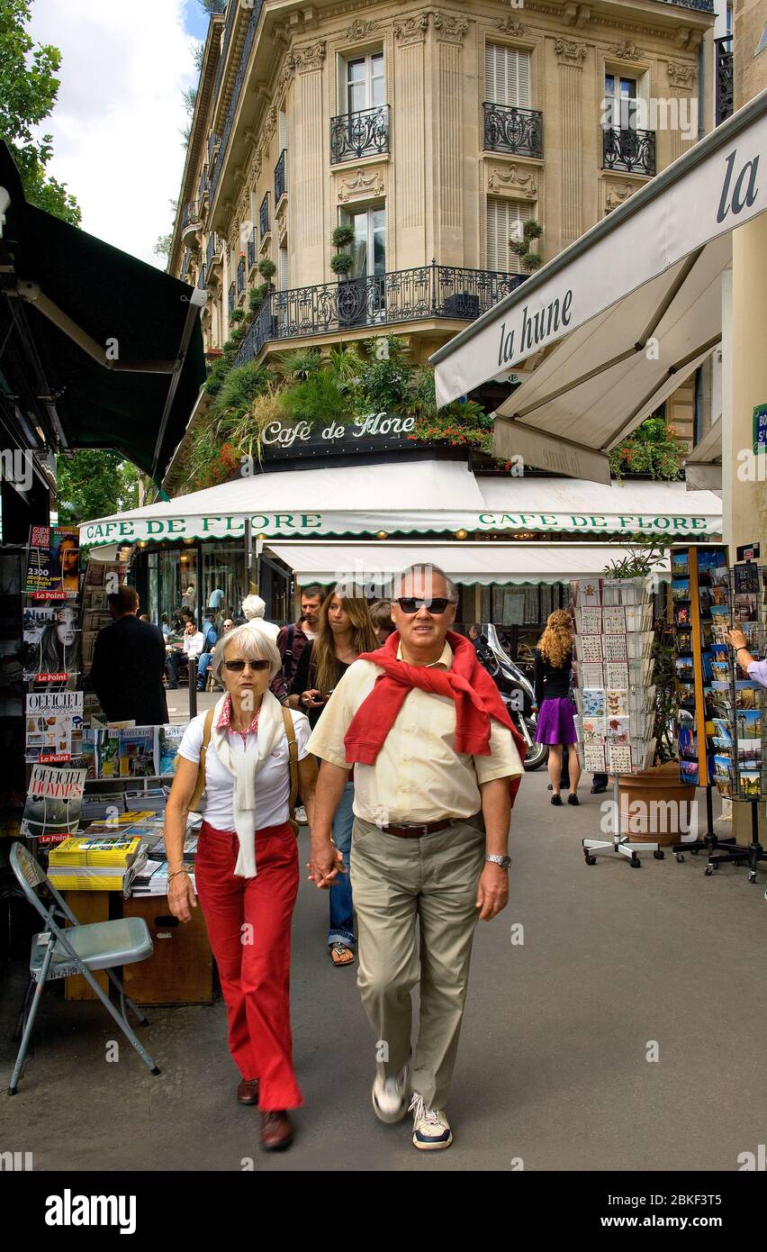 Streetscene in Paris with a couple in Boulevard StGermain  with Cafe de Flore in the background and a paper stall on the left in the foreground, Paris Stock Photo
